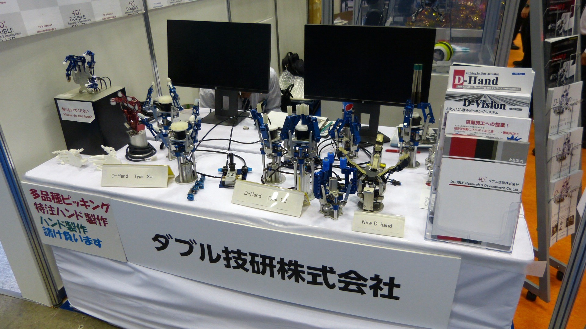 a counter of robot hands of various metallic colours with pamphlets for D-Hand and D-Vision